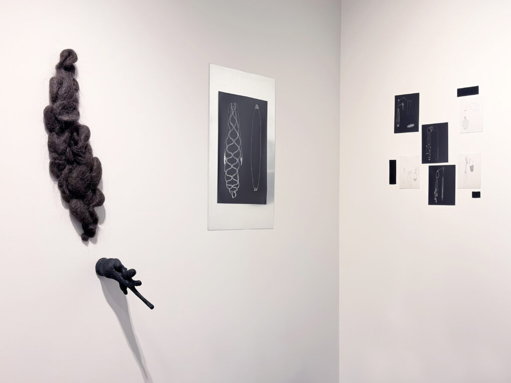 L'Ombre du corps, 2026. Galerie Le Trécarré, N-É. Photo C Patenaude // 2025. Cheveux, fil. 75 x 30 x 10 cm. // 2025. Gant de laine, acrylique. 18 x 15 x 21.5 cm. // 2026. 1 photo-dessin, feuille d’aluminium. 66,5 x 40,5 cm // 2026. 6 photos-dessins. Total : 52 x 41 cm.